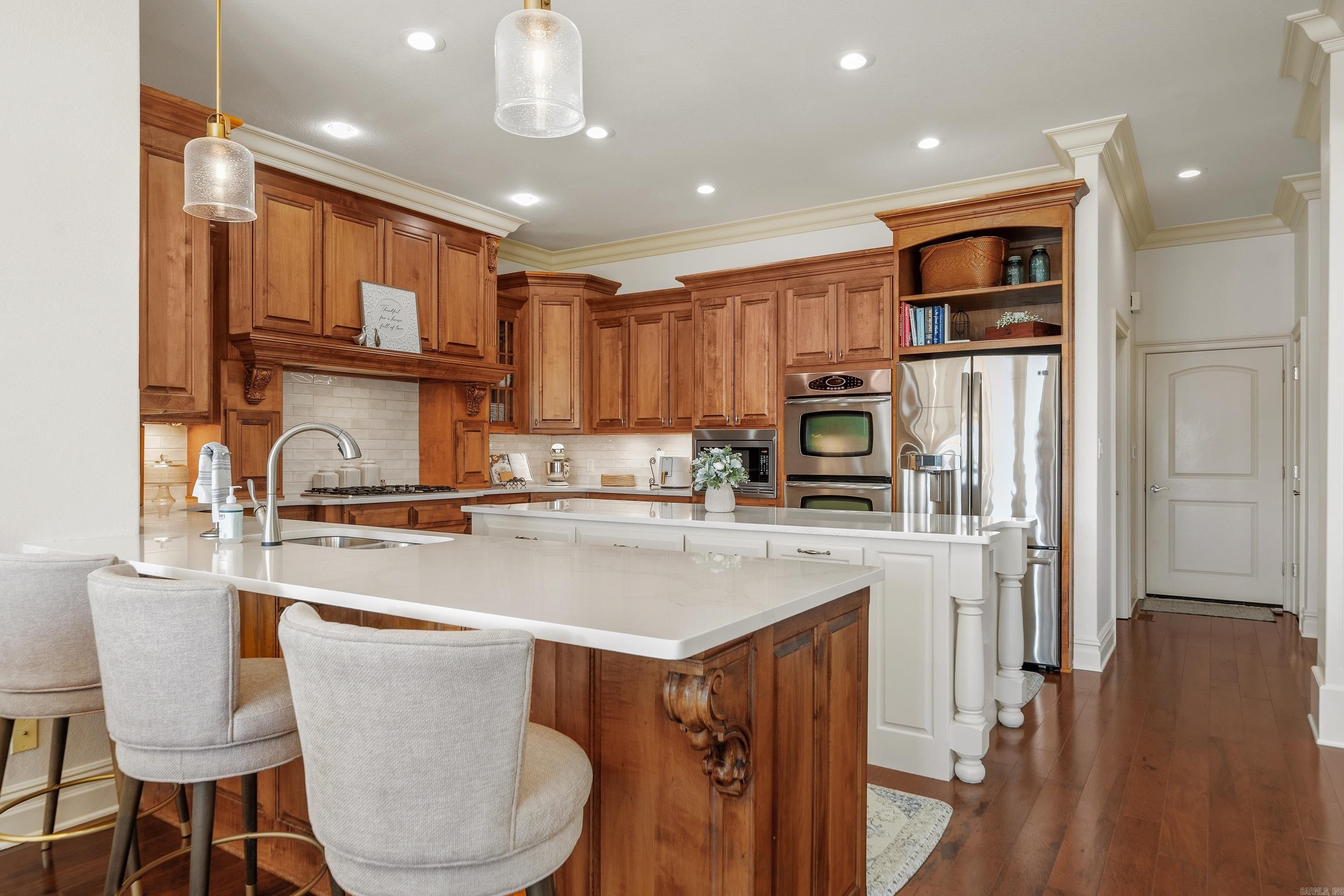 Kitchen with warm wood cabinets, a large white island, upholstered stools, and stainless steel appliances.