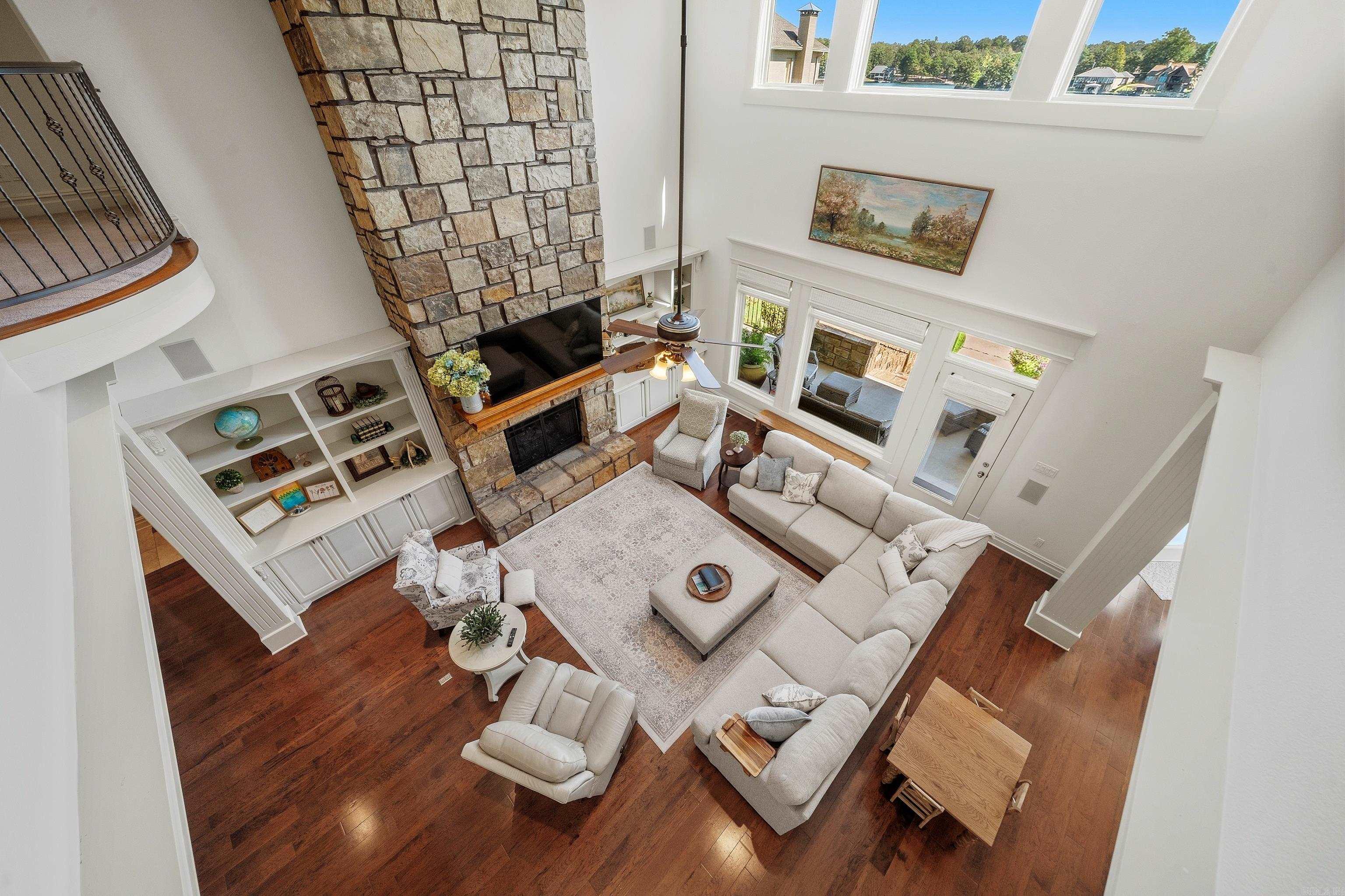 Living room with a towering stone fireplace, pale sectional, hardwood floors, and windows overlooking the lake.