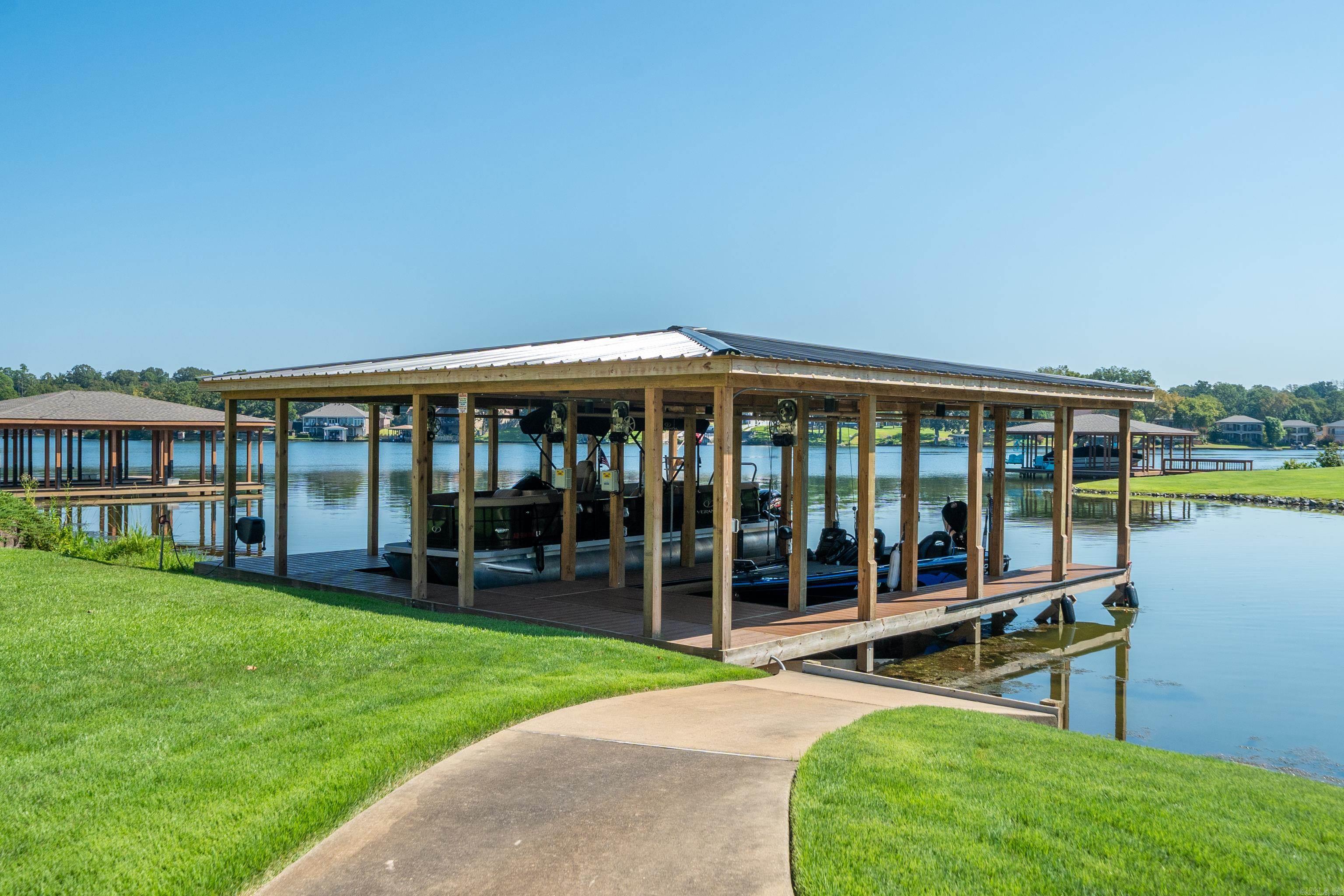 Covered boat dock with boats on a lake, reached by a walkway across a green lawn.