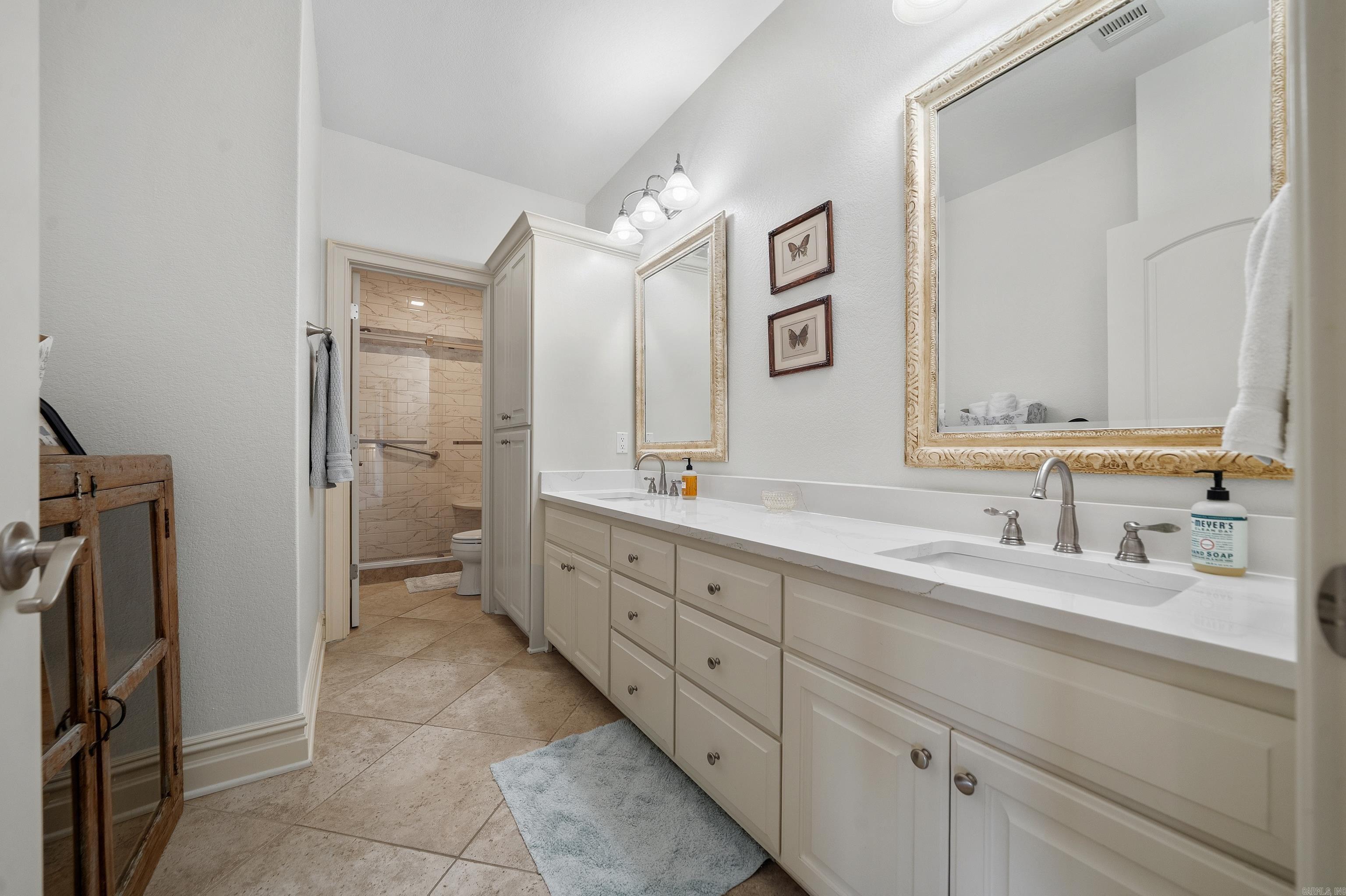 Bathroom with a long double vanity, large framed mirrors, and a tiled shower at the back.