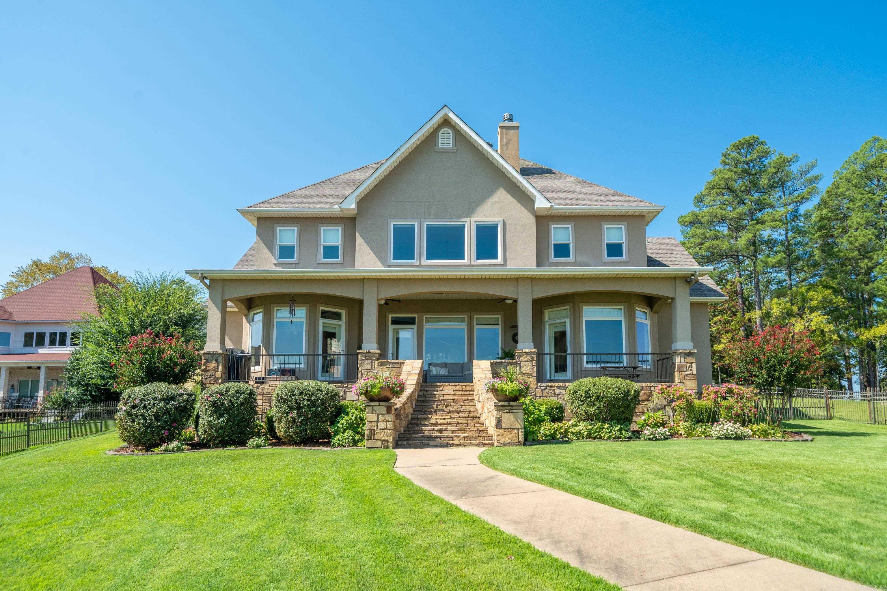 Two-story stucco house with a stone-fronted porch, landscaped garden, and curved walkway.