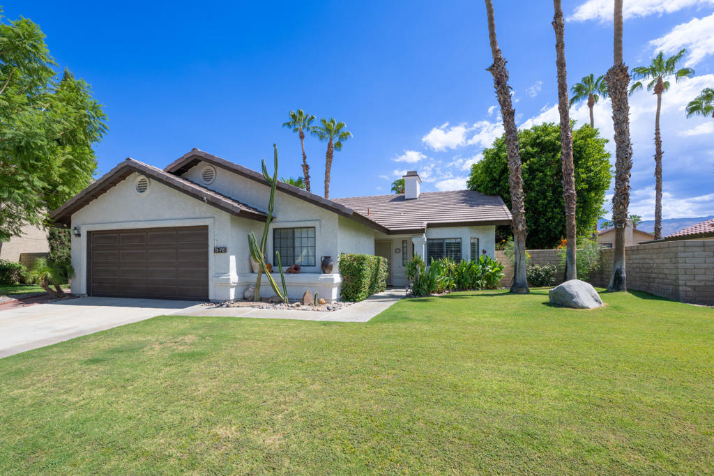 Single-story home with a two-car garage, cactus landscaping, palm trees, and a broad lawn.