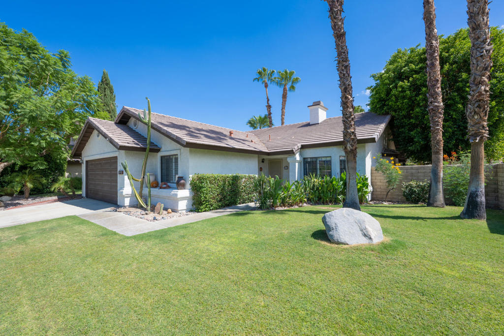Single-story stucco home with an attached garage, palm trees, and a broad green lawn.