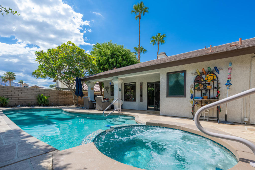 Backyard pool and bubbling circular spa beside the home, with patio seating and palm trees.