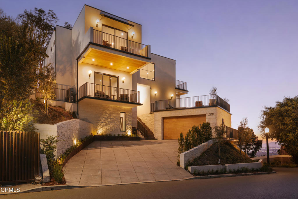 Modern multi-level home at dusk with illuminated balconies and a broad paved driveway.