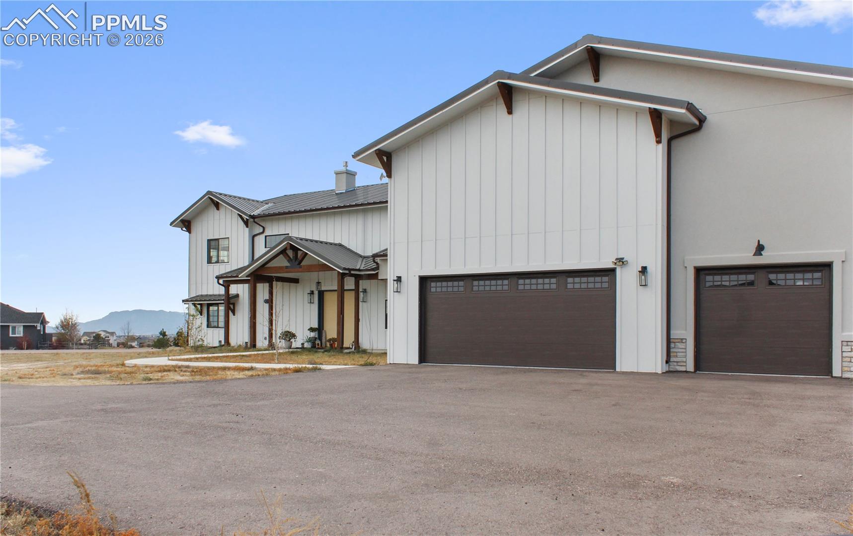 White modern farmhouse with two dark garage doors and distant mountains.
