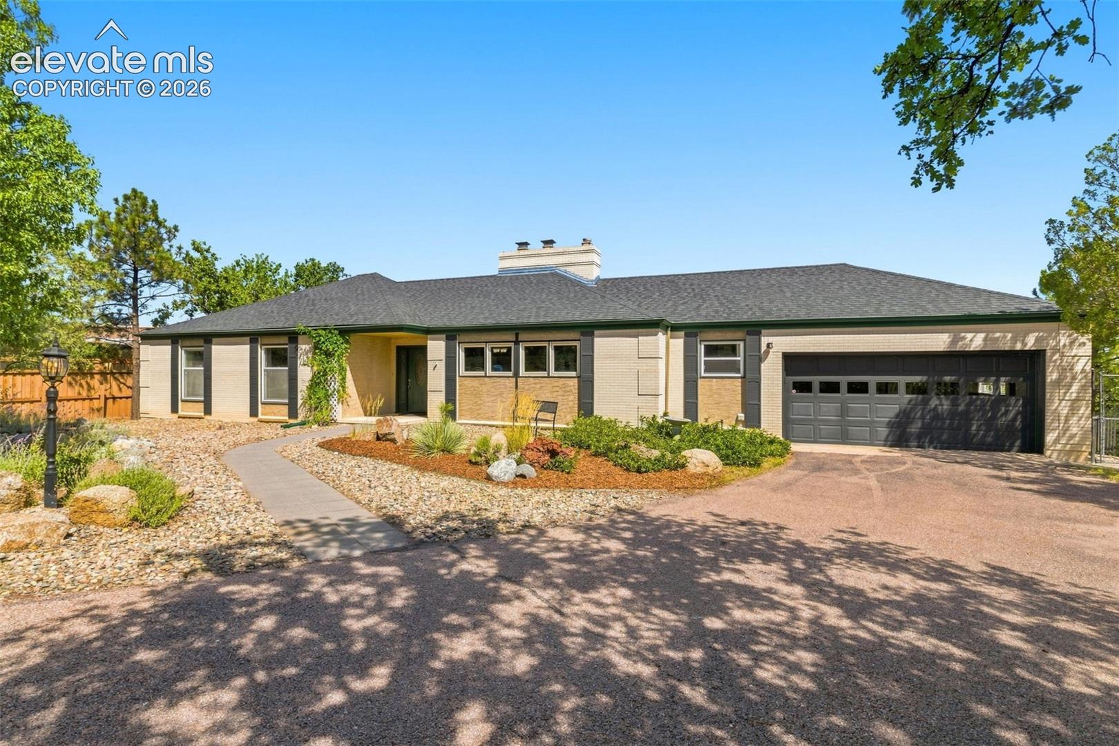 Single-story brick home with a dark roof, attached garage, and landscaped front yard.
