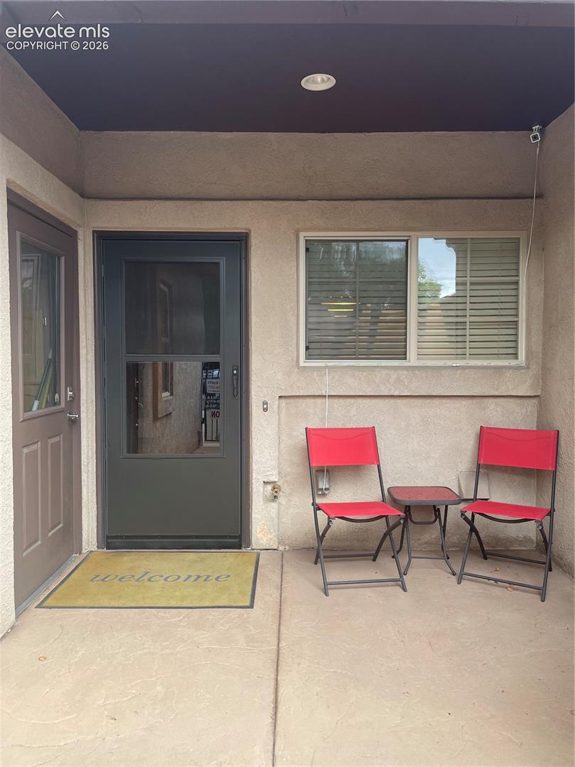 Covered home entry patio with two red folding chairs, a small table, and a welcome mat.