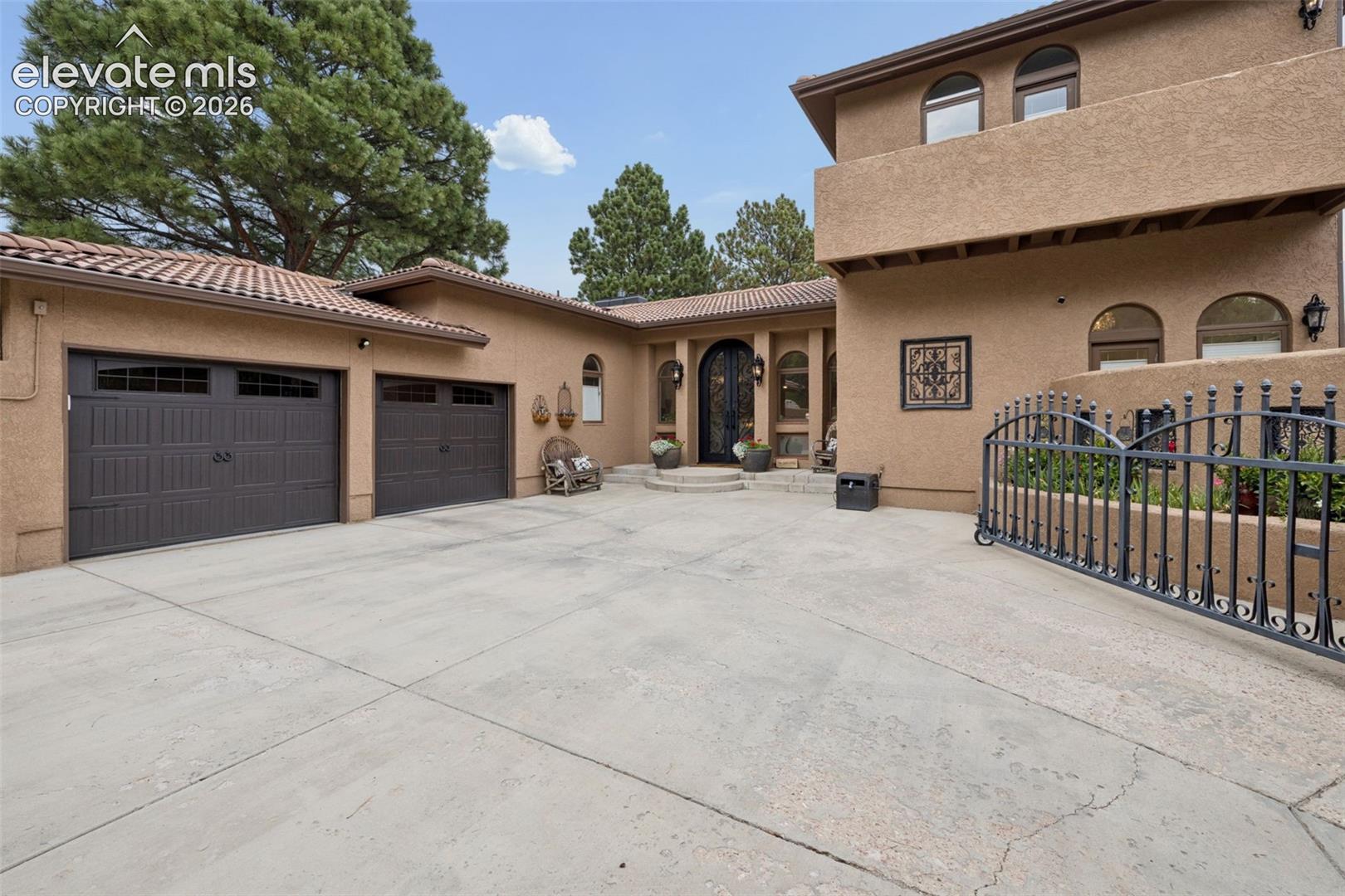 Tan stucco home with two garage doors, a broad driveway, and a black metal gate.