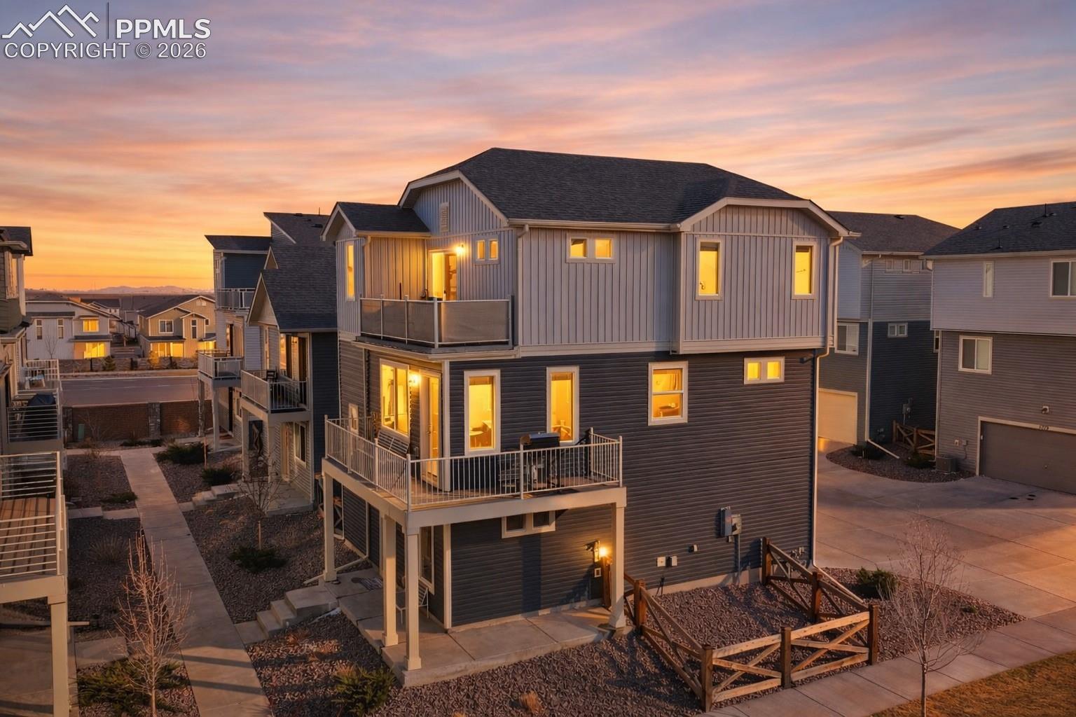 Multi-story gray home with two balconies and glowing windows at sunset.