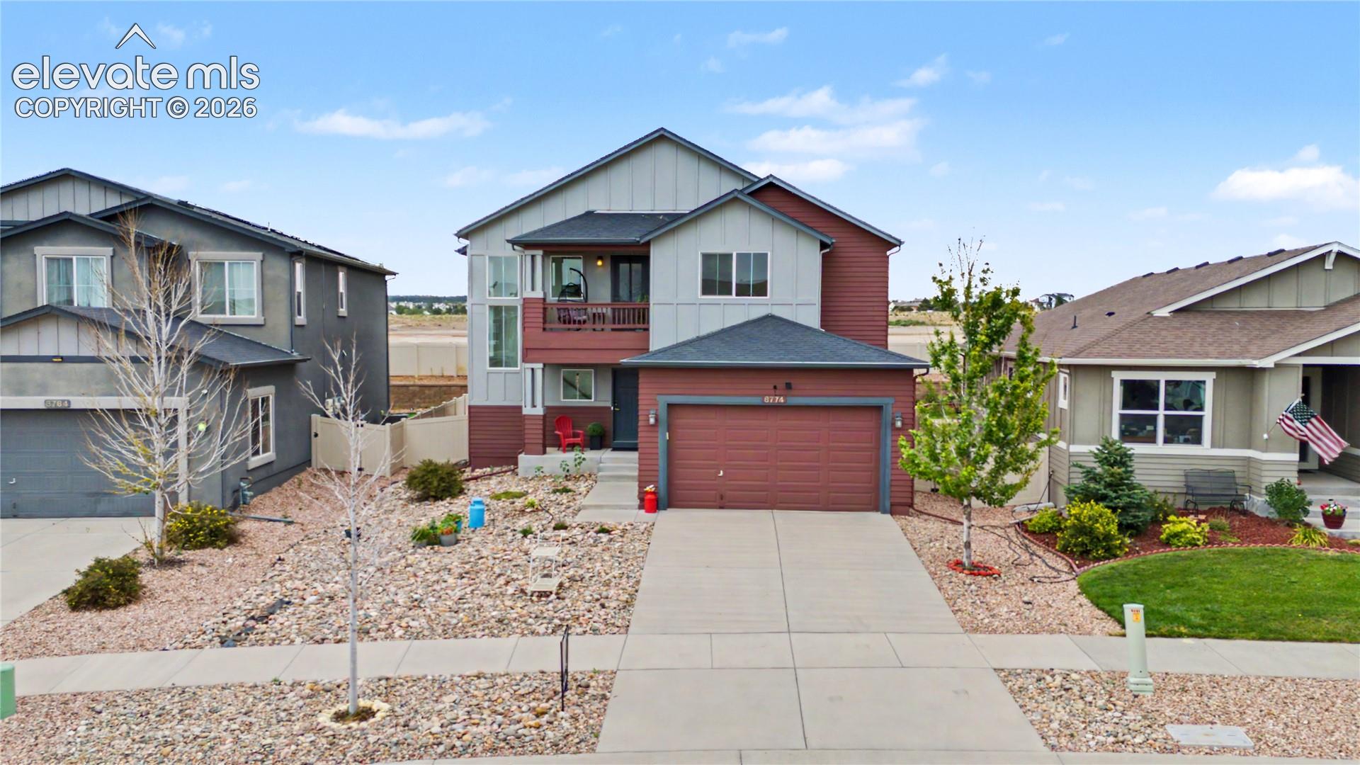 Two-story gray and red house with a covered balcony, two-car garage, and rock landscaping.