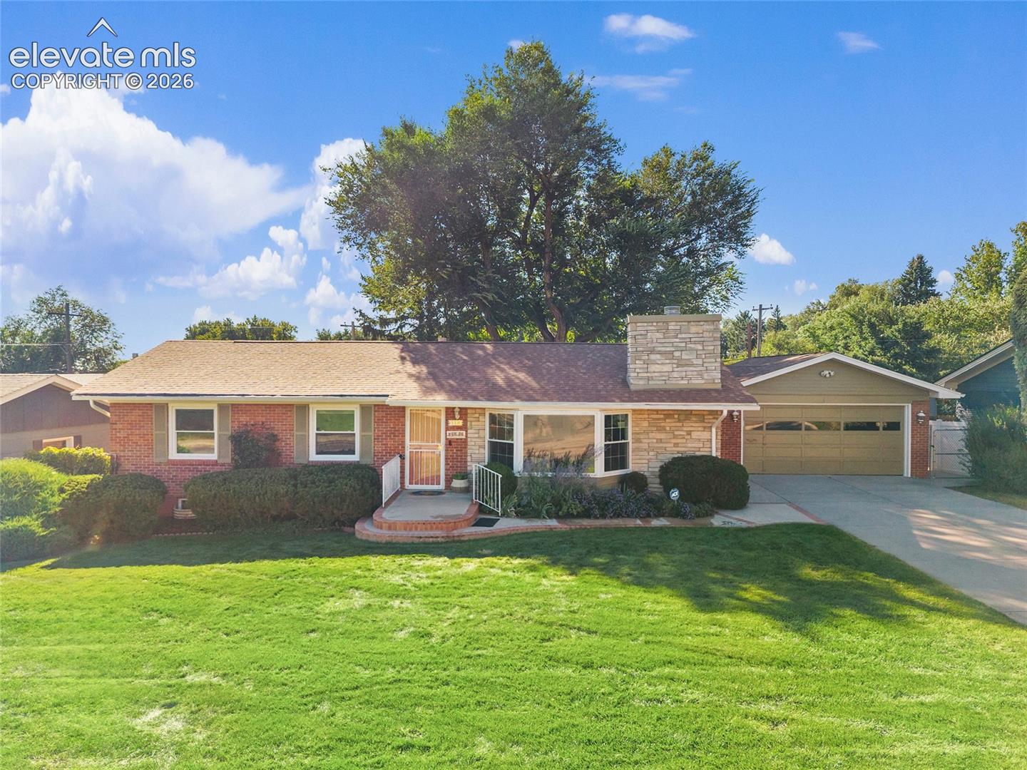 Single-story brick ranch house with a stone chimney, attached garage, and broad green lawn.