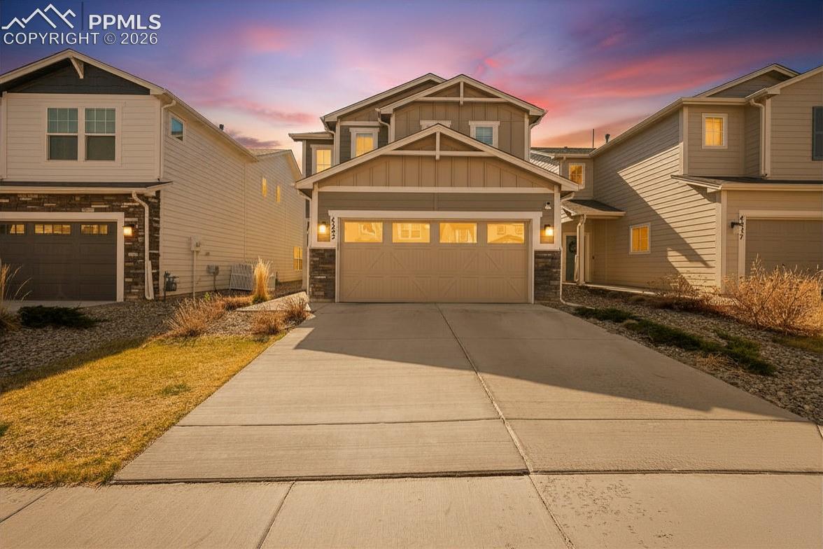 Two-story home with an attached garage and broad driveway beneath a pink sunset.