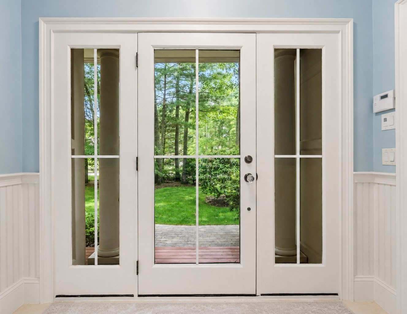 Front entry with a white glass-paneled door opening visually onto a leafy garden and stone walkway.