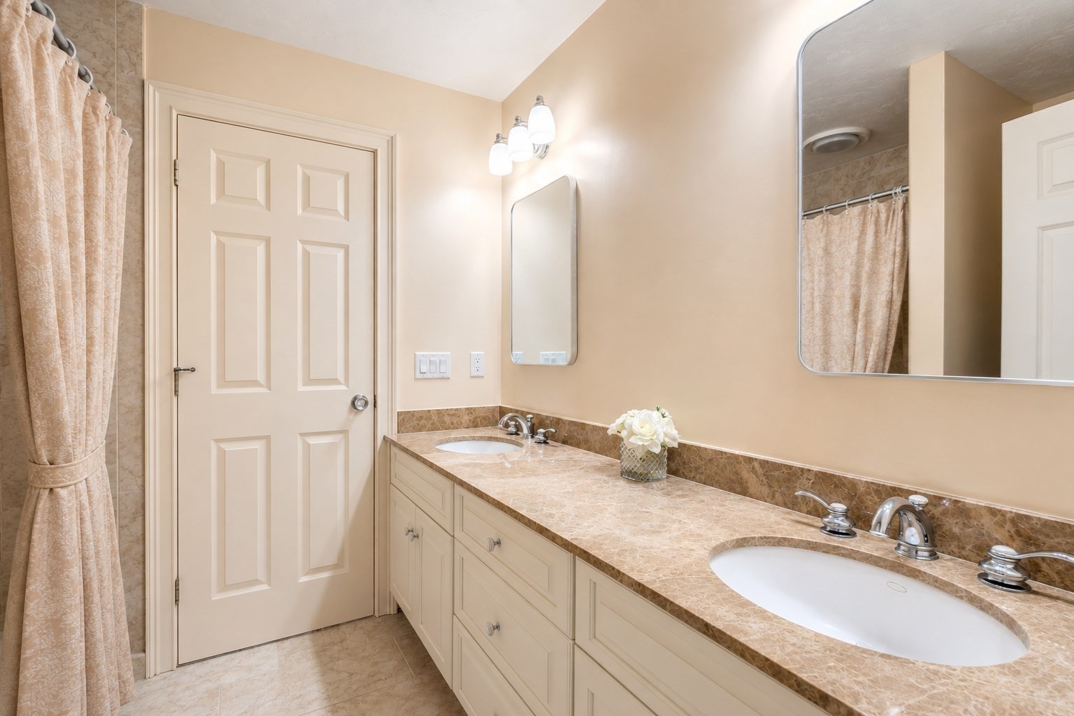 Bathroom with a long double-sink vanity, beige stone-pattern counters, and a curtained shower.