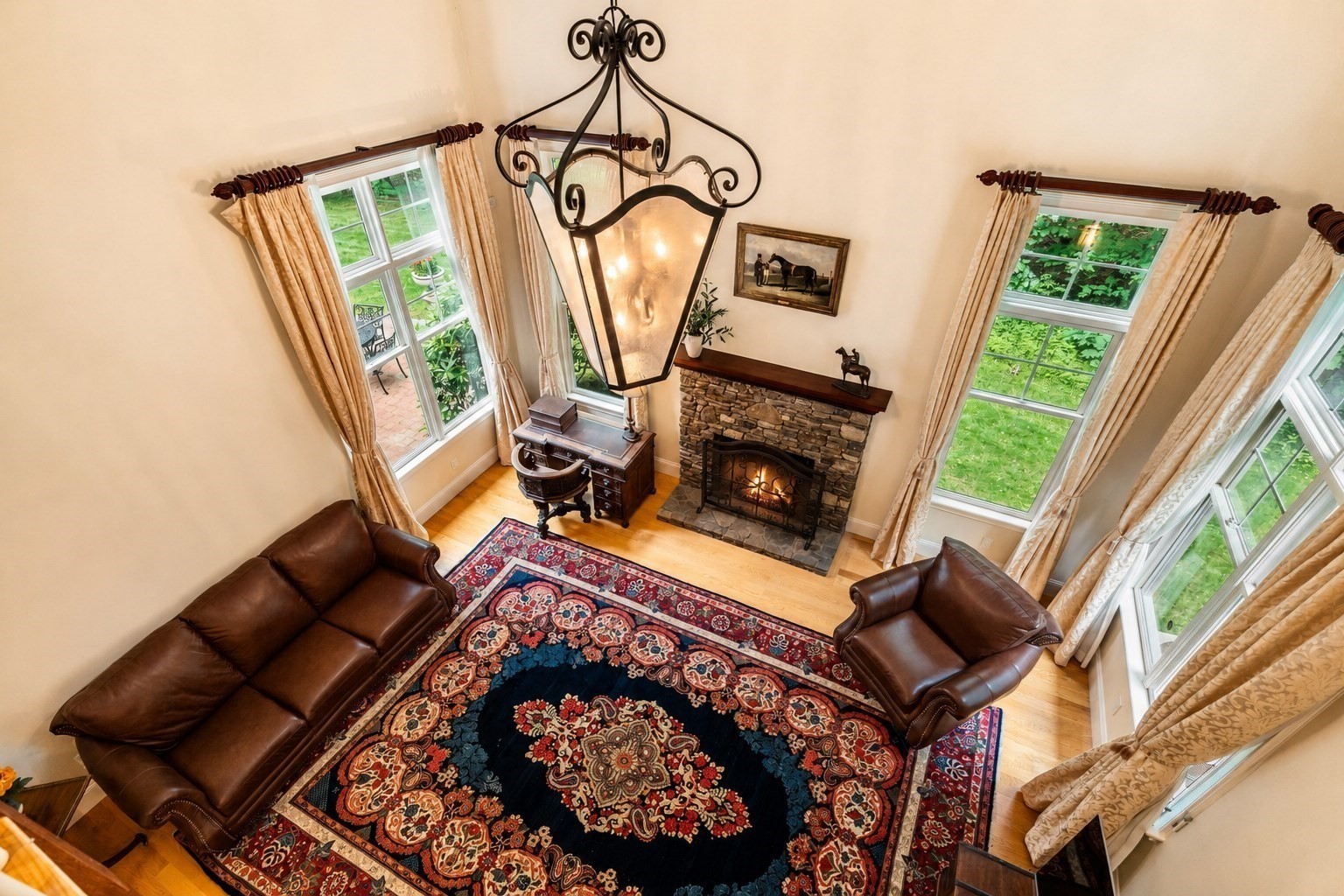 Vaulted living room with a stone fireplace, wrought-iron chandelier, leather seating, and patterned rug.