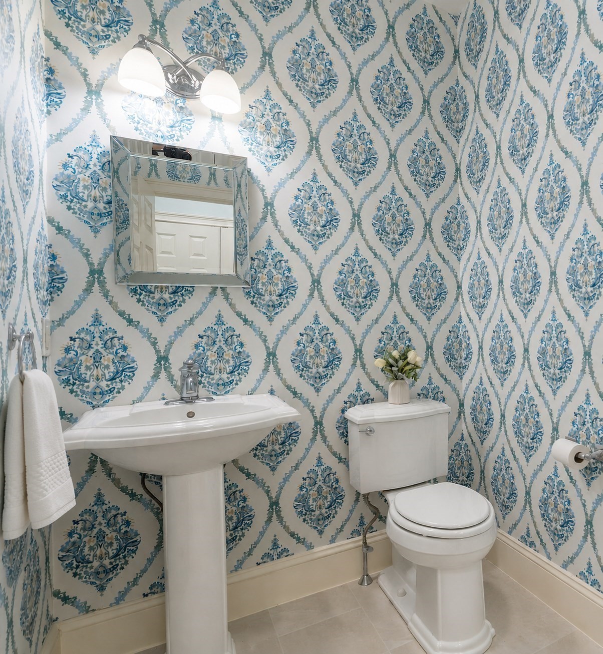 Powder room with ornate blue patterned wallpaper, a pedestal sink, and a white toilet.