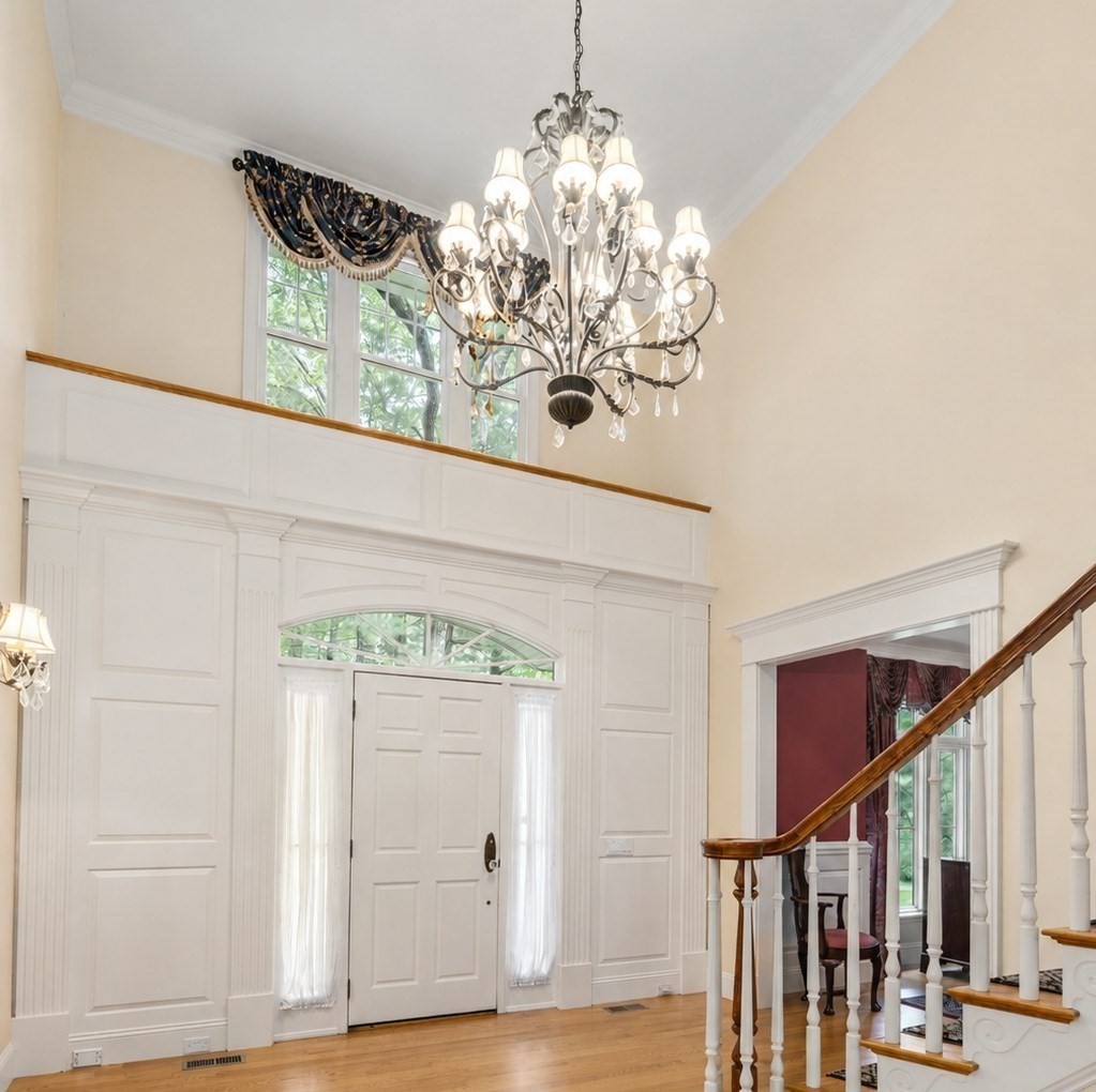 Two-story foyer with a paneled entry, arched windows, ornate chandelier, and curved staircase.