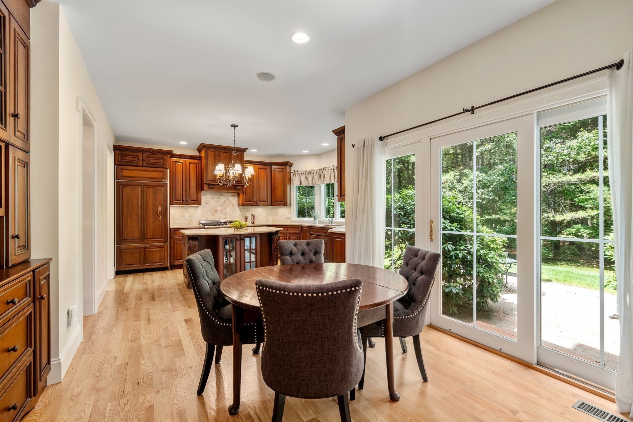 Kitchen and dining area with rich wood cabinetry, a round table, and glass doors overlooking greenery.