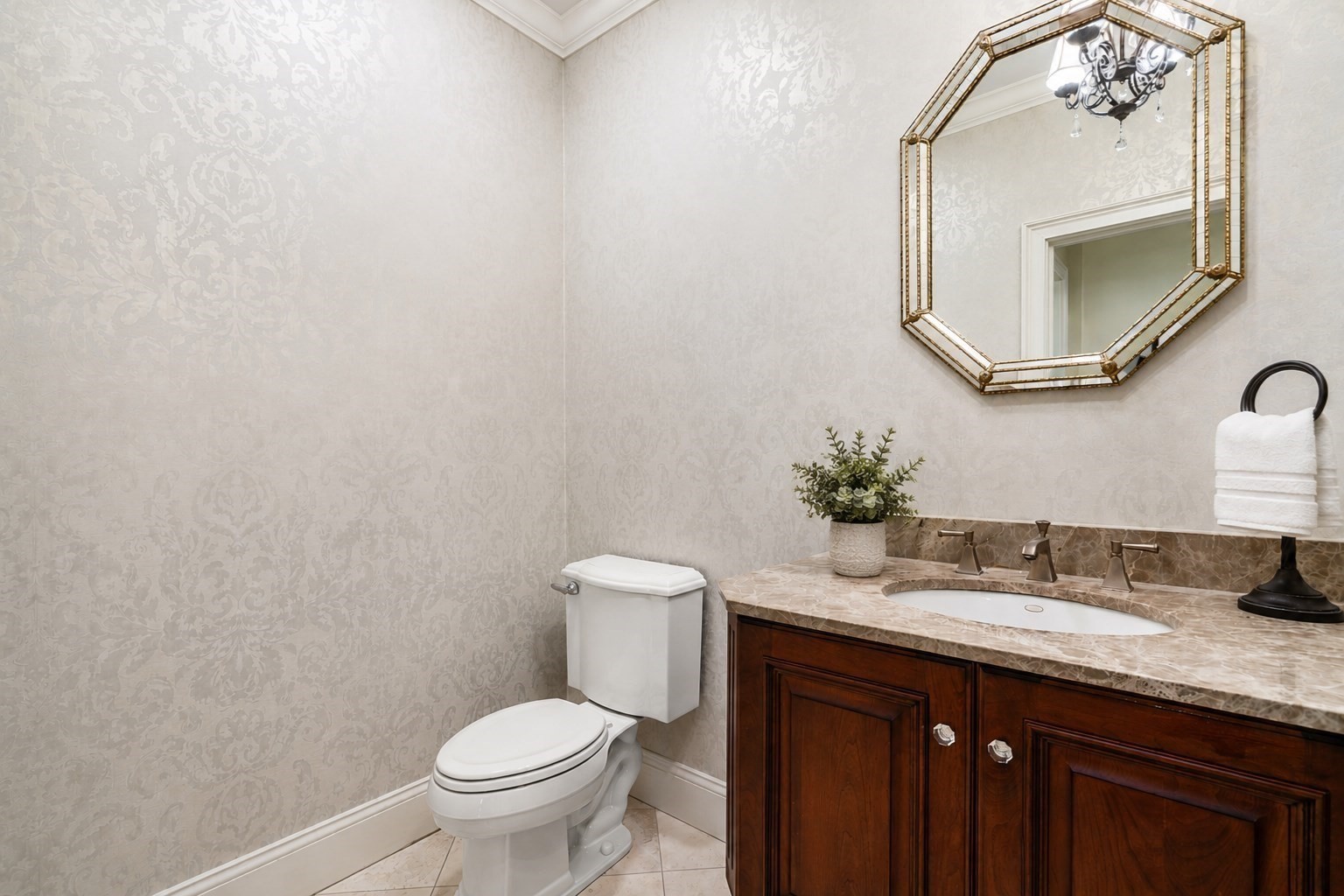 Powder room with patterned wallpaper, a marble vanity, and an angular gold-framed mirror.