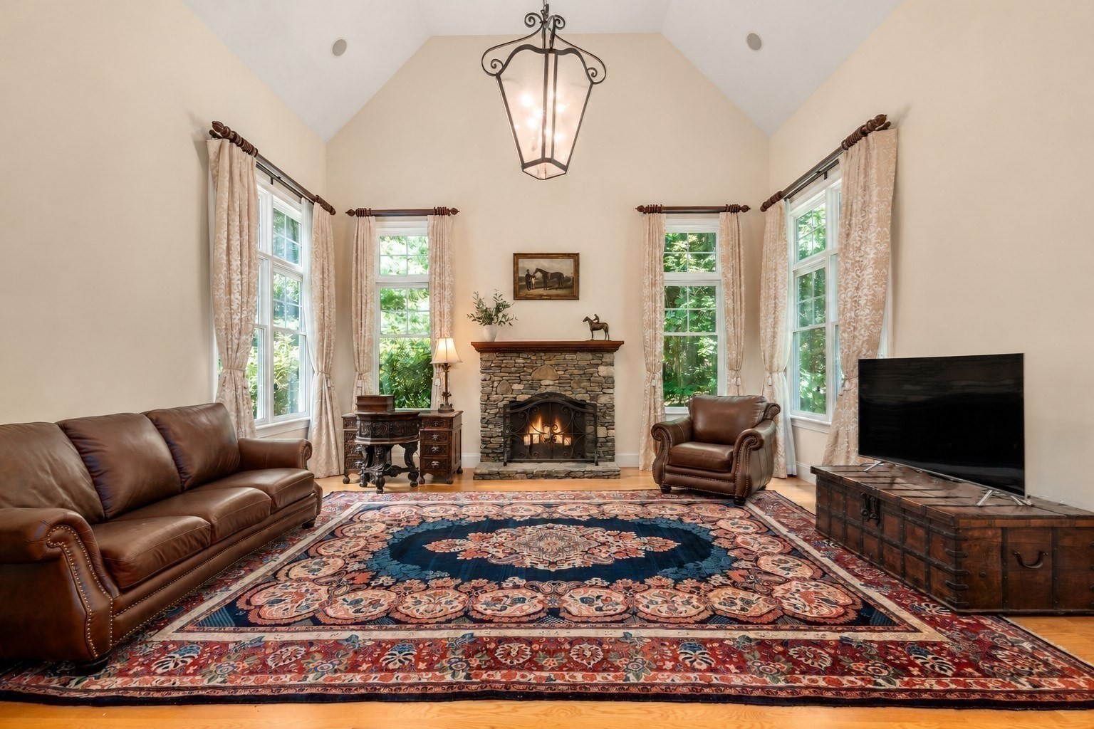 Living room with a vaulted ceiling, stone fireplace, leather seating, and tall curtained windows.