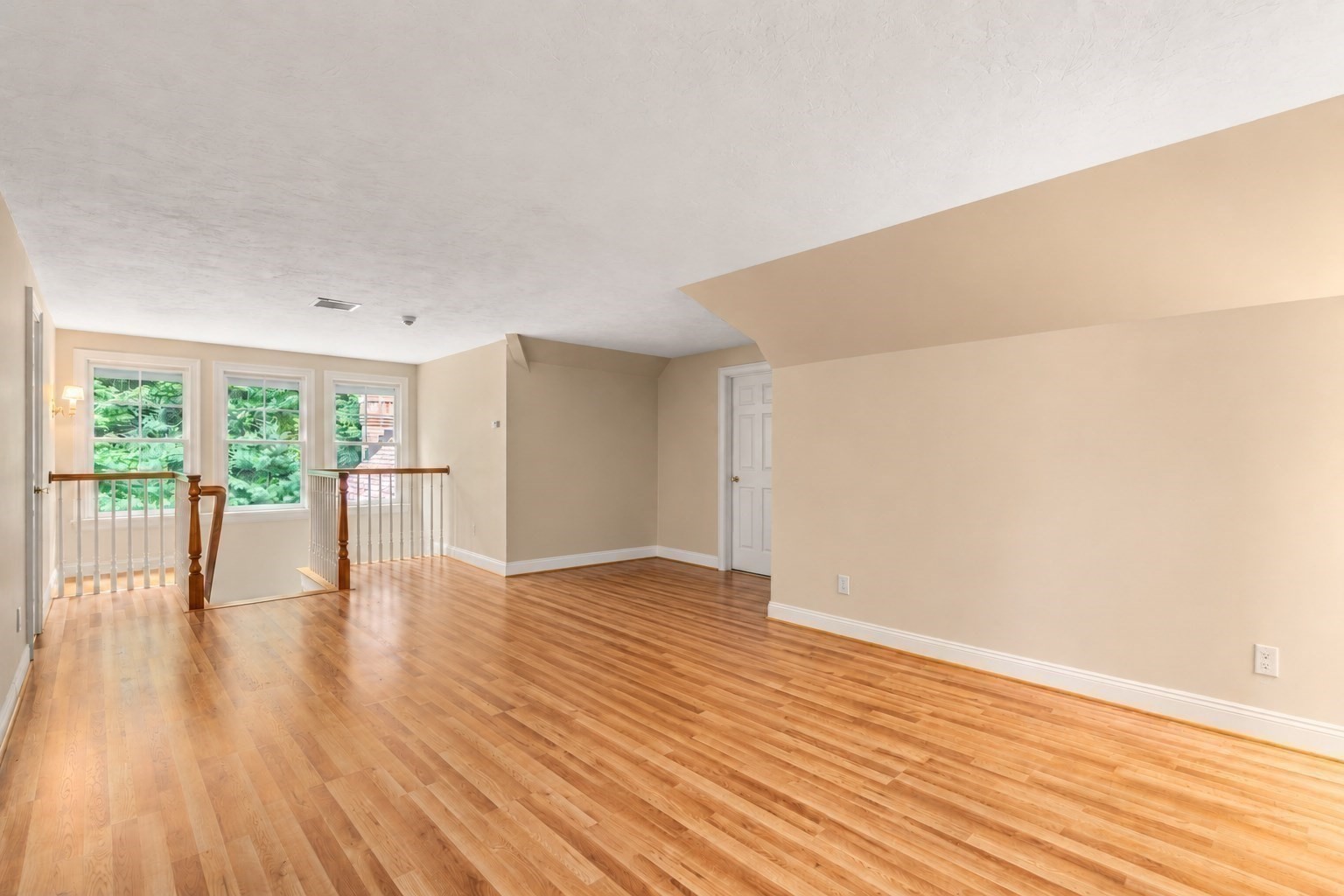 Empty upstairs living area with hardwood floors, three windows, and a stair railing.