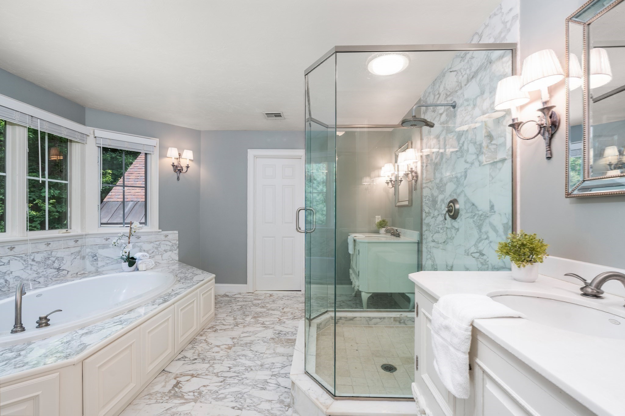 Bathroom with a marble-clad soaking tub, glass shower, and white vanity.