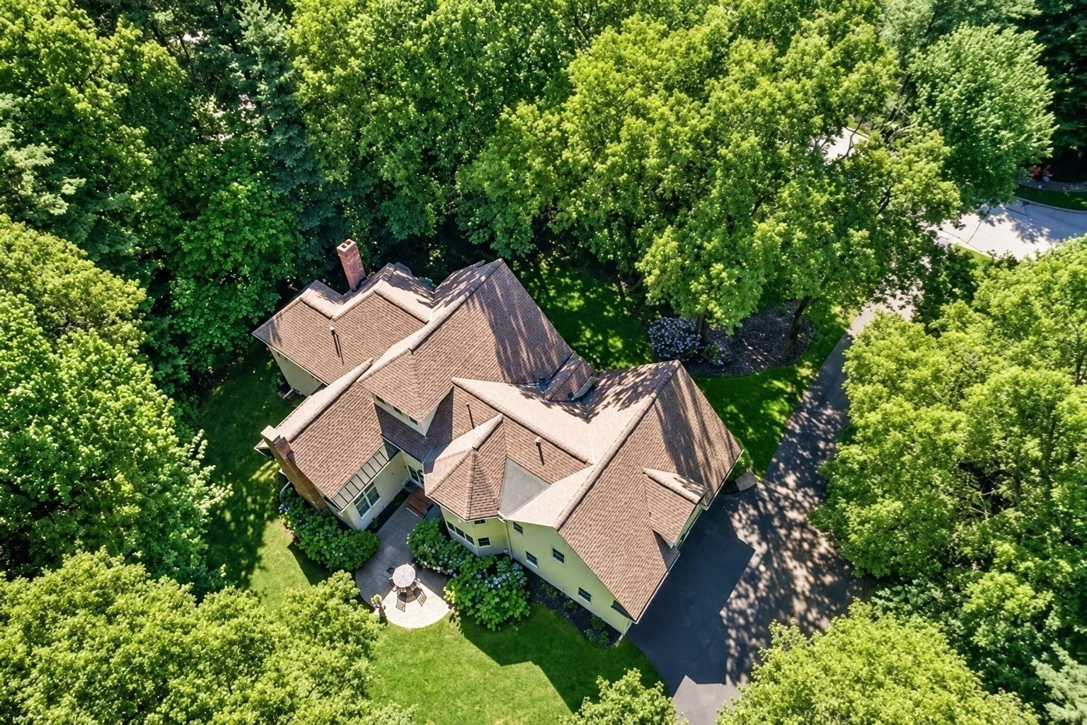 Aerial view of a large tree-surrounded home with a multi-gabled roof and curved driveway.