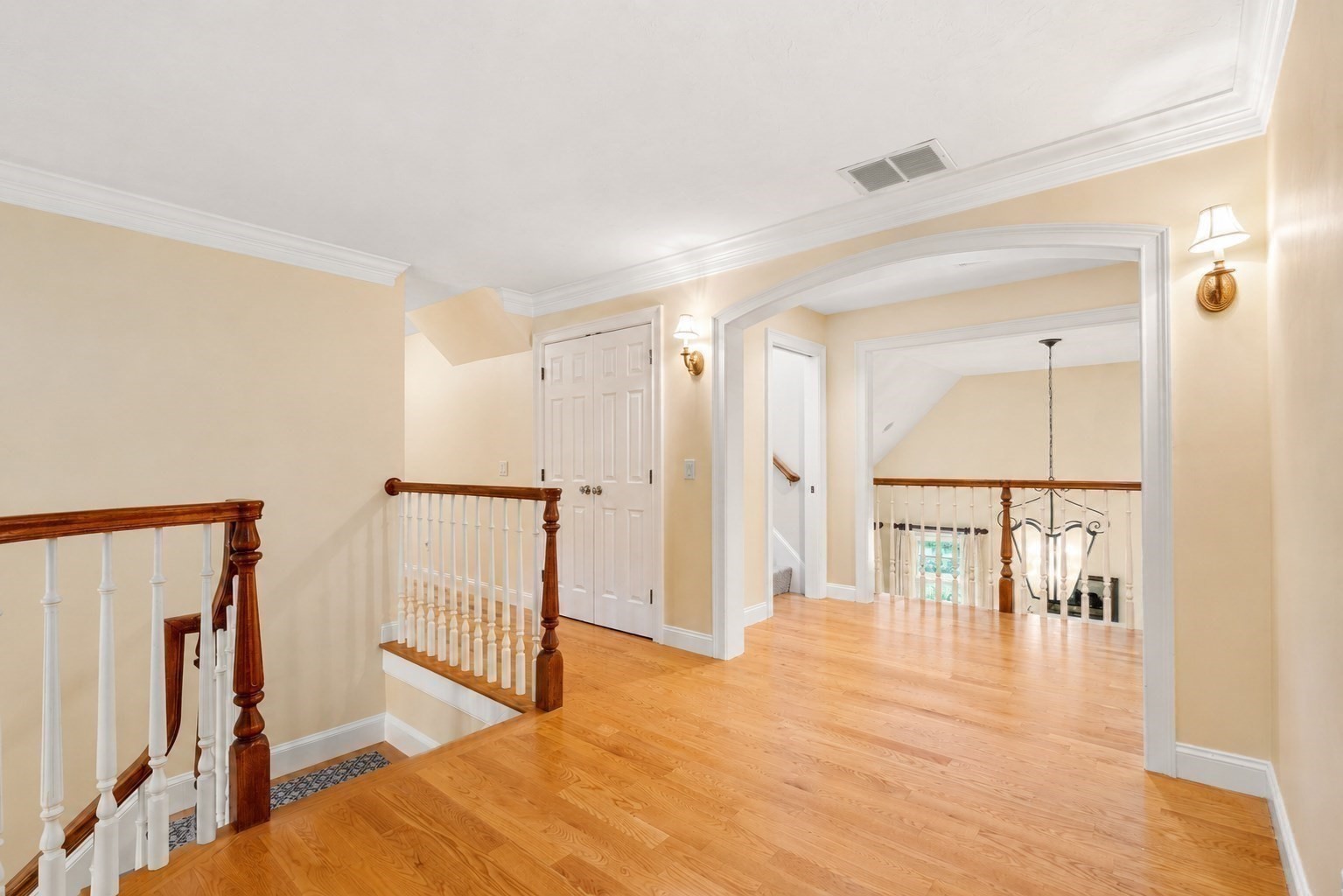 Upstairs landing with hardwood floors, an arched opening, and dark wood stair railings.