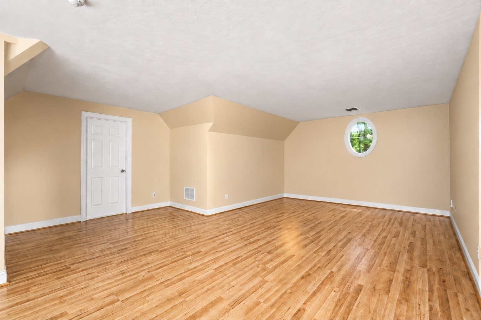 Empty room with polished hardwood floors, angled ceiling, and a small round window.