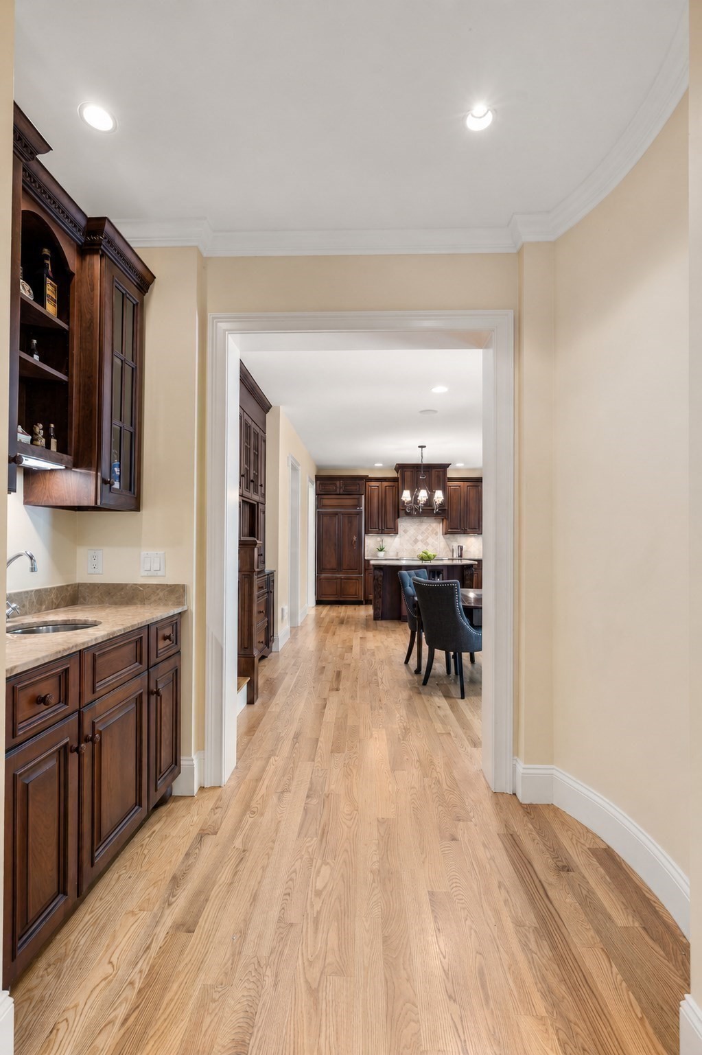Hardwood-floored passage with dark cabinetry opening onto a kitchen and dining area.