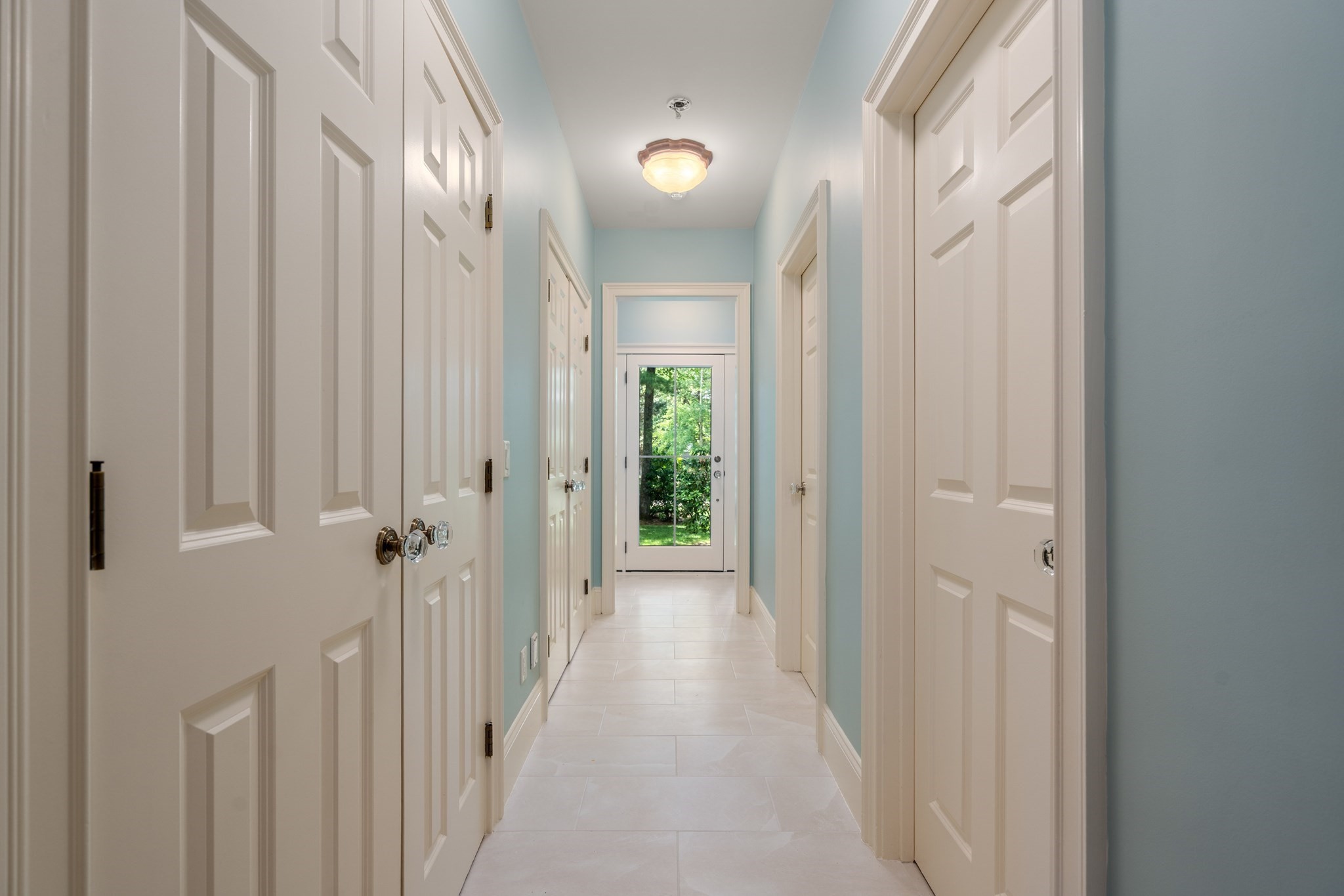 Hallway with pale blue walls, white paneled doors, and a tiled floor leading to a glass door.