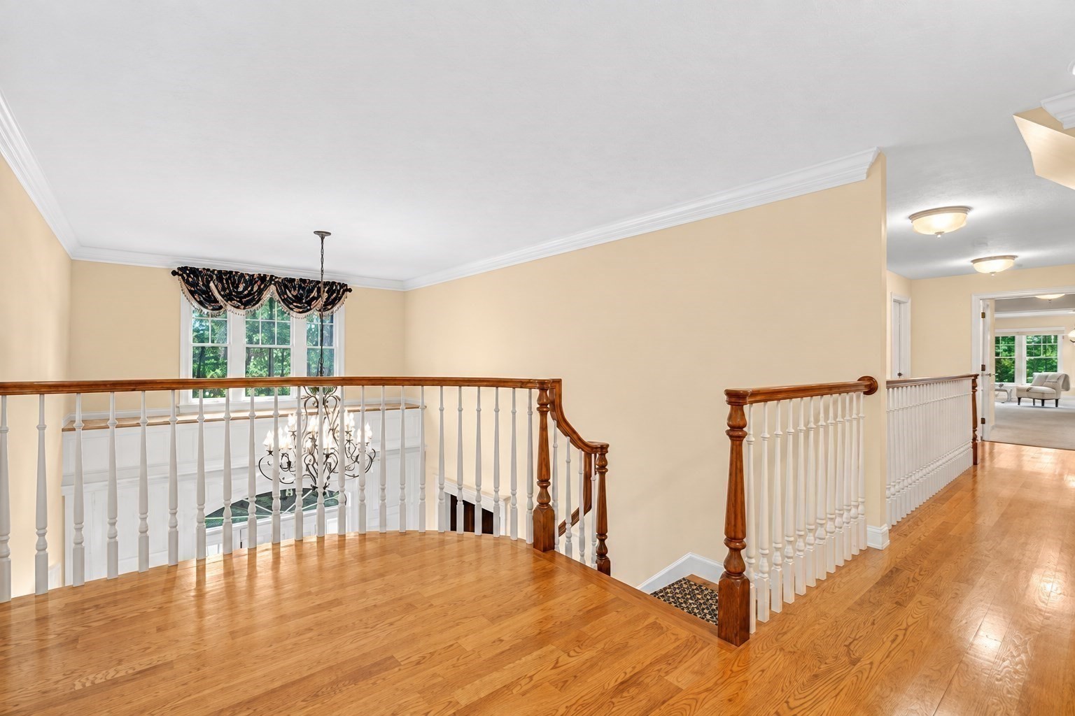 Upstairs landing with hardwood floors, white railings, a chandelier, and a window overlooking greenery.