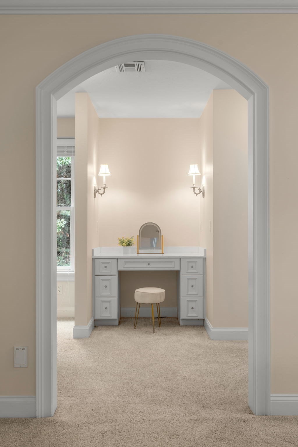 Dressing area with a white built-in vanity and stool, framed by a wide arched doorway.