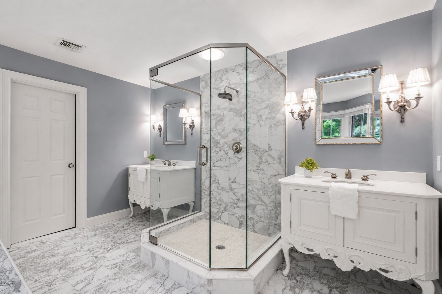 Bathroom with a marble walk-in shower and two ornate white vanities.