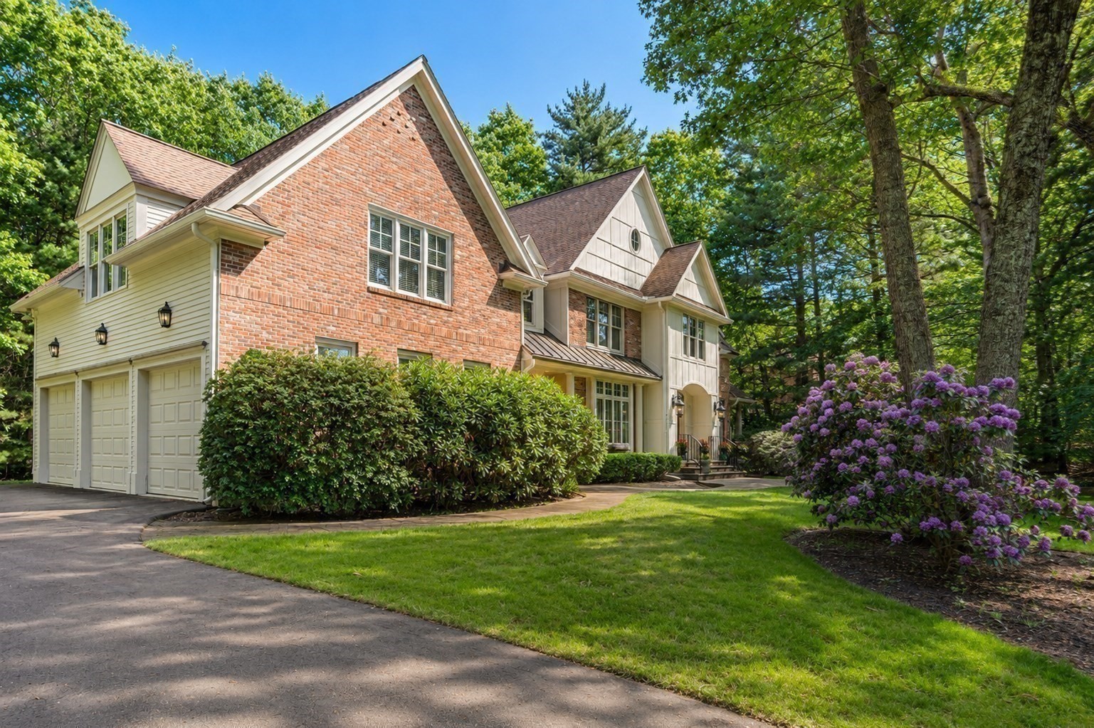 Two-story brick and cream-sided home with a three-car garage and purple flowering shrubs.