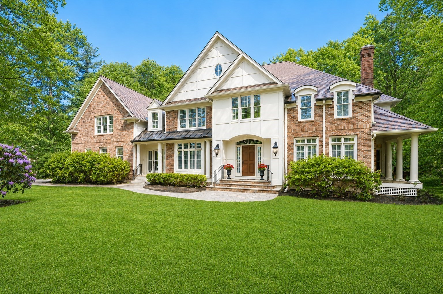 Large brick-and-white house with a covered porch, landscaped shrubs, and a broad green lawn.
