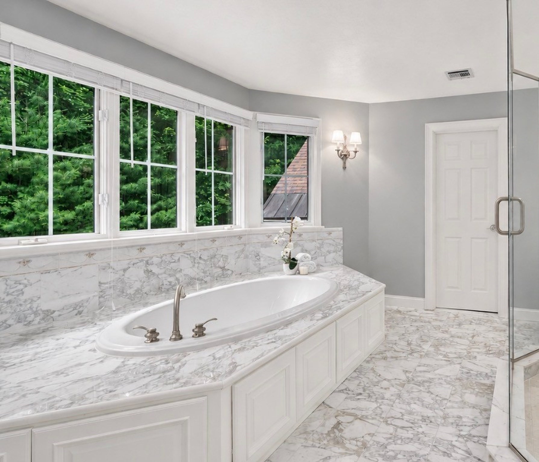 Bathroom with an oval soaking tub, marble surfaces, glass shower, and windows overlooking greenery.