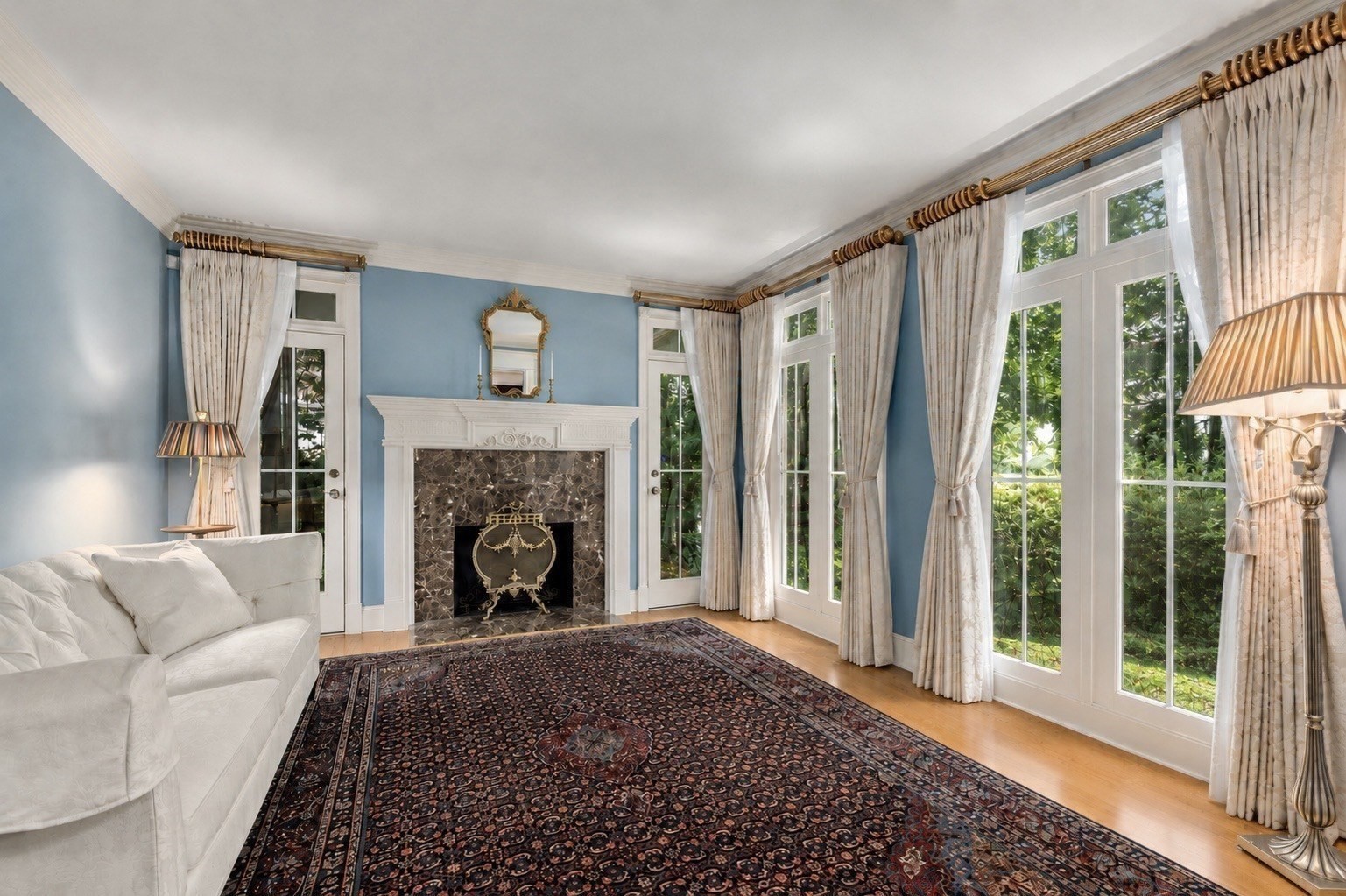 Living room with a white fireplace, blue walls, tall curtained windows, and a patterned rug.