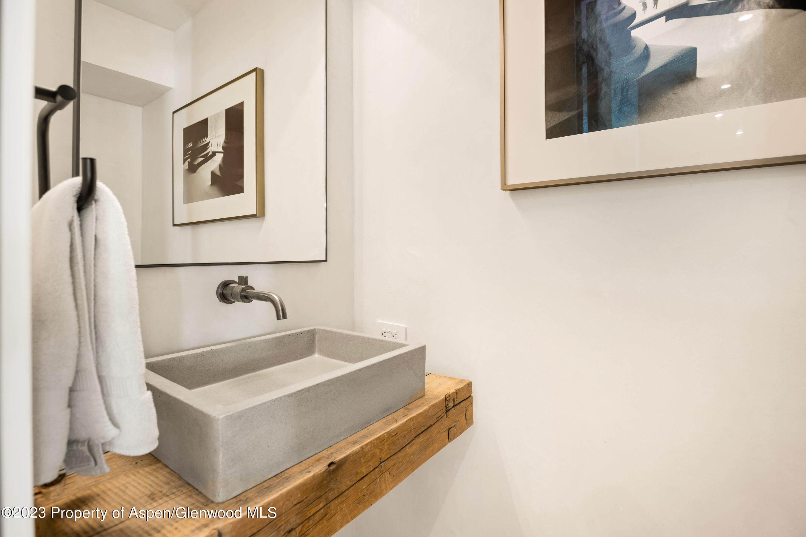 Bathroom vanity with a concrete vessel sink, wall-mounted faucet, and rustic wood countertop.