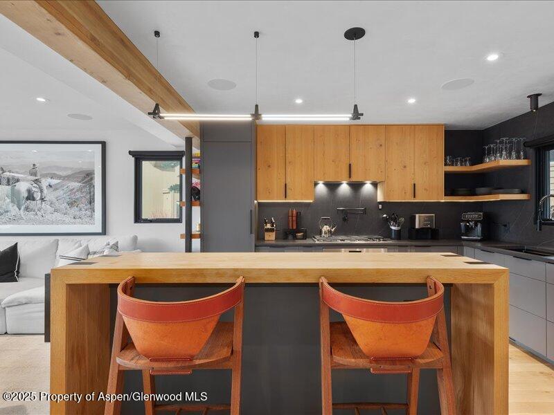 Open-plan kitchen with warm wood cabinetry, a large island, and two orange leather bar stools.