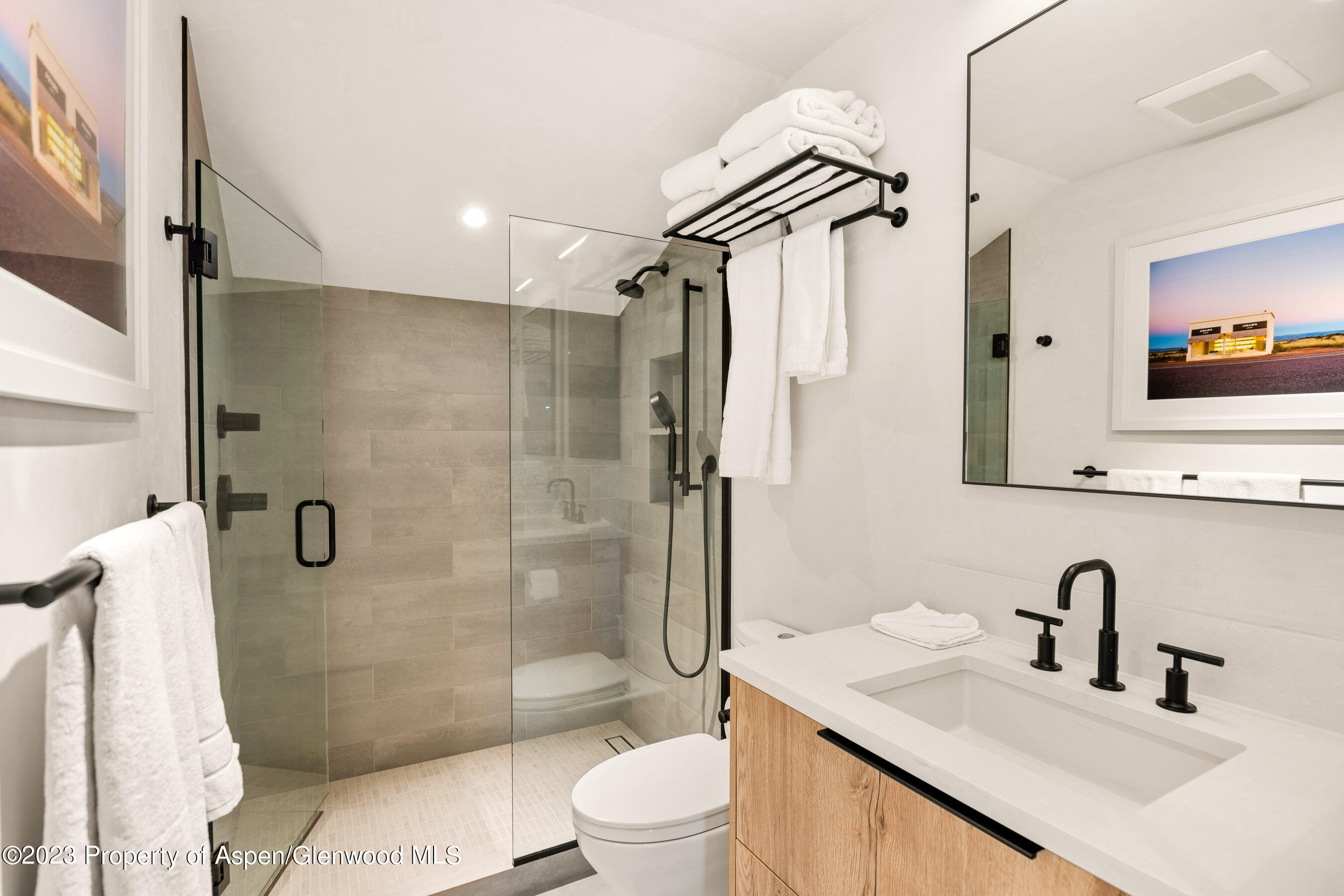 Modern bathroom with a glass walk-in shower, black fixtures, and a wood-front vanity.