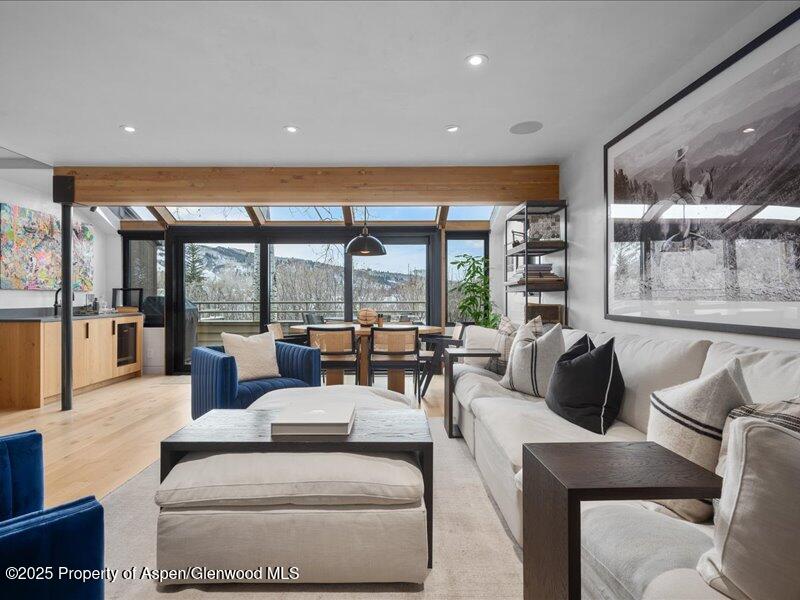 Living room with a long white sofa, blue armchairs, and large windows overlooking trees and mountains.