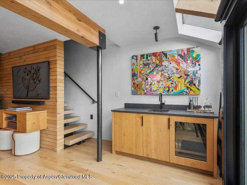 Modern kitchenette with colorful abstract artwork beside an open staircase and wood-paneled partition.