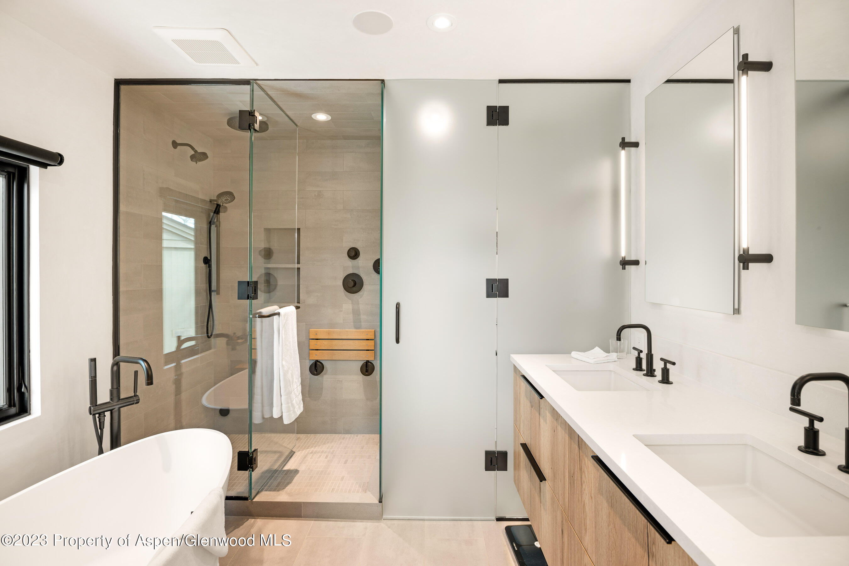 Modern bathroom with a glass shower, freestanding tub, and double wood vanity.