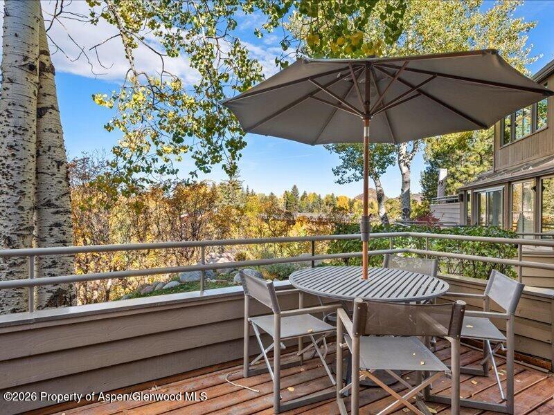 Outdoor deck with dining table and umbrella overlooking colorful autumn trees.