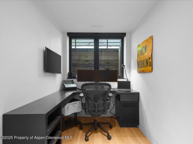 Compact home office with a wraparound desk, mesh chair, and window overlooking a wooden fence.