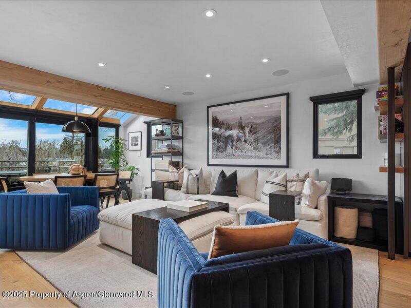 Living room with a cream sectional, blue velvet chairs, and wood-framed skylights.