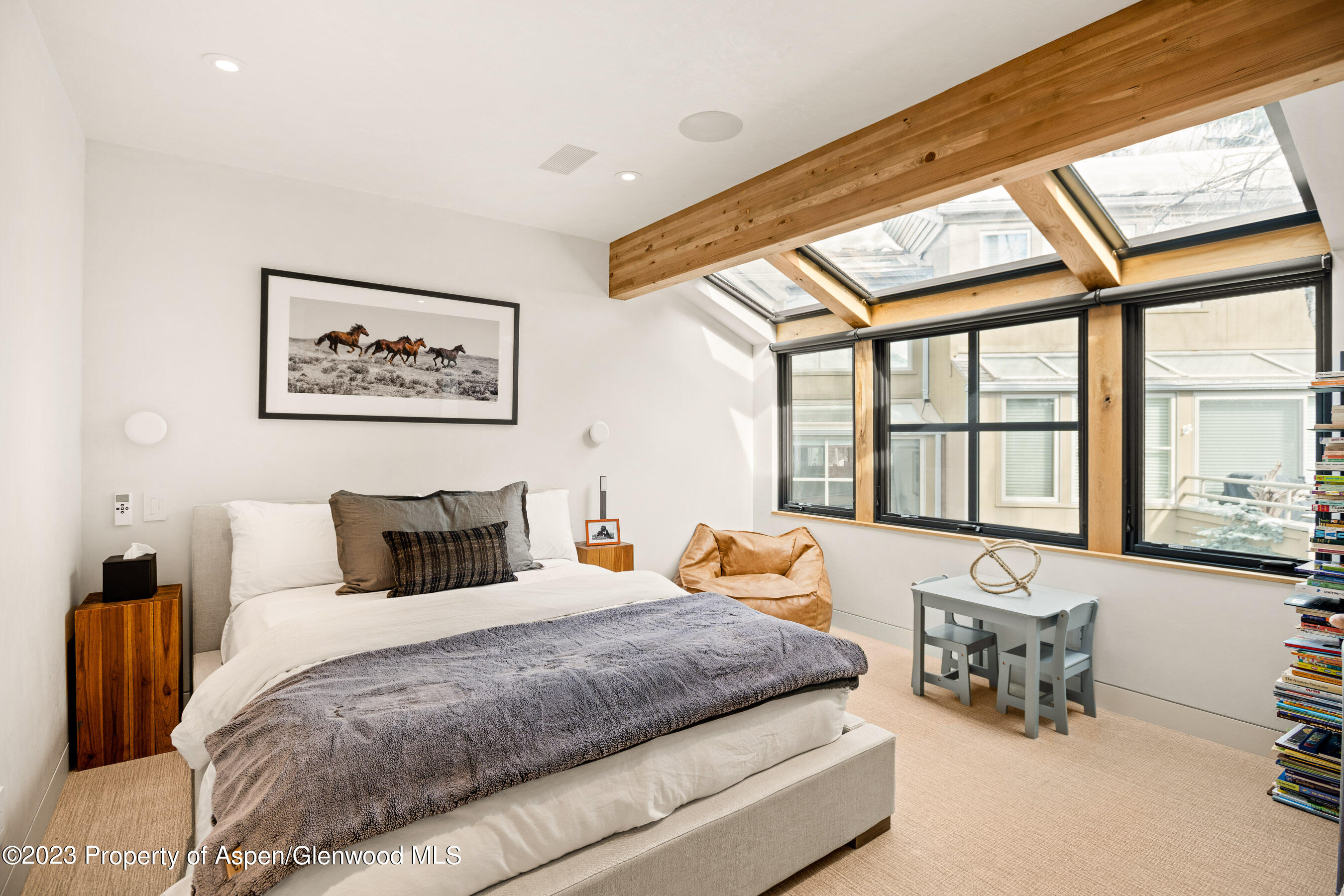 Furnished bedroom with exposed timber beams, skylights, and large black-framed windows.