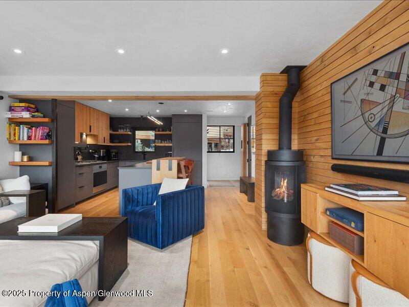 Open-plan living room with a blue chair, black fireplace, wood-paneled wall, and kitchen.